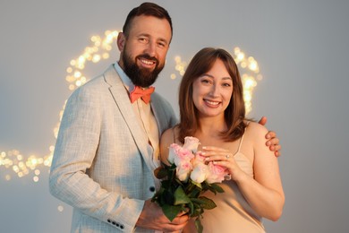 Photo of Making marriage proposal. Woman with engagement ring, flowers and her fiance on light grey background, bokeh effect