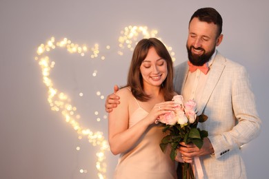 Photo of Making marriage proposal. Woman with engagement ring, flowers and her fiance on light grey background, space for text. Bokeh effect