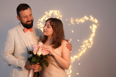 Photo of Making marriage proposal. Woman with engagement ring, flowers and her fiance on light grey background, space for text. Bokeh effect