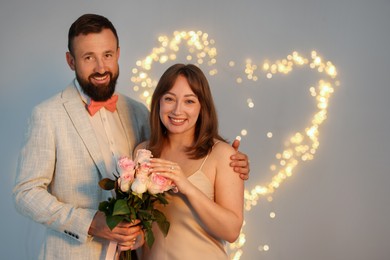Photo of Making marriage proposal. Woman with engagement ring, flowers and her fiance on light grey background, space for text. Bokeh effect