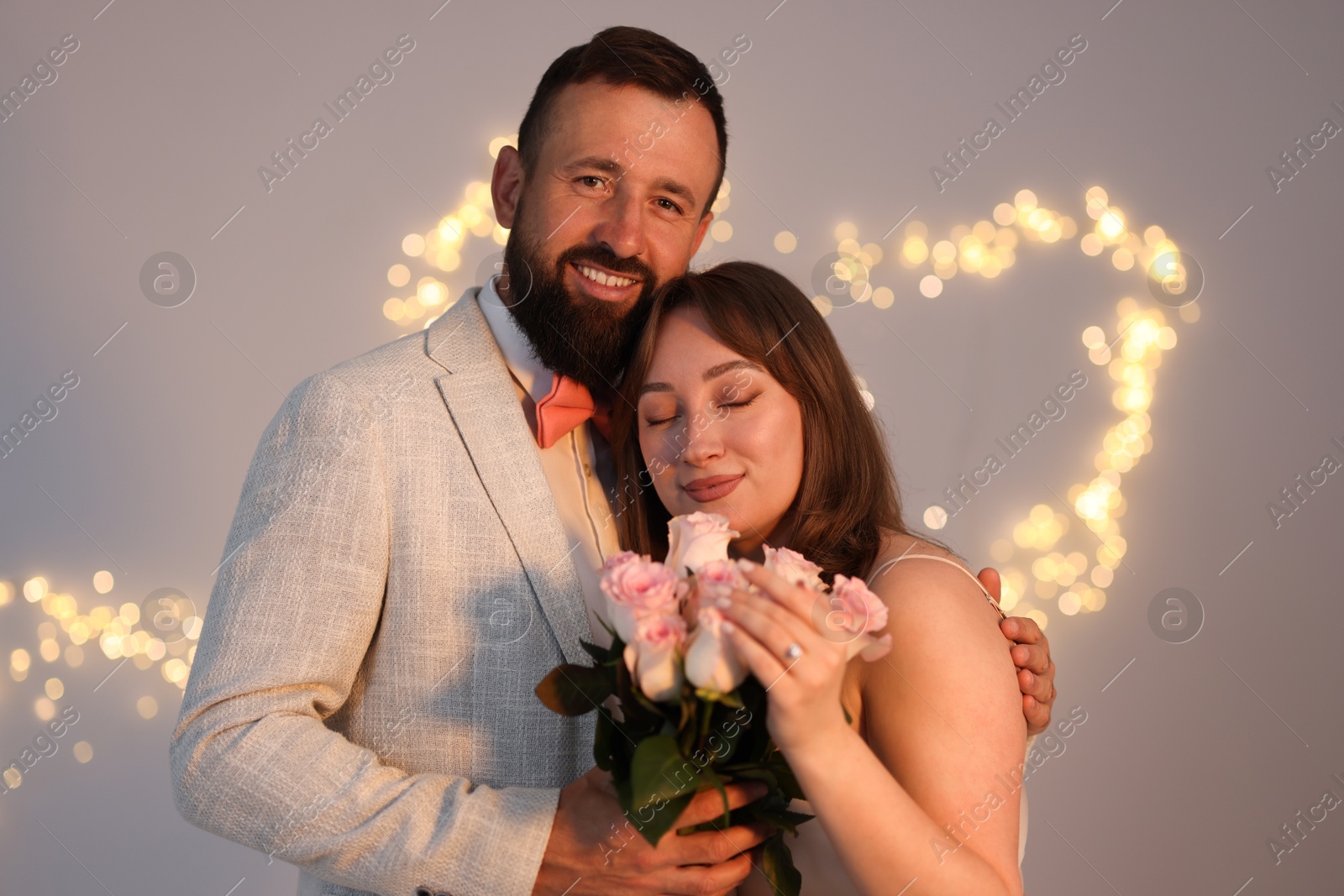 Photo of Making marriage proposal. Woman with engagement ring, flowers and her fiance on light grey background, bokeh effect