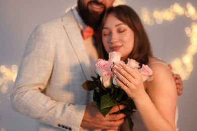 Photo of Making marriage proposal. Woman with engagement ring, flowers and her fiance on light grey background, selective focus. Bokeh effect