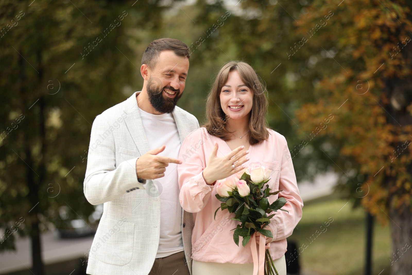 Photo of Making marriage proposal. Woman with engagement ring, flowers and her fiance outdoors