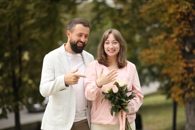 Photo of Making marriage proposal. Woman with engagement ring, flowers and her fiance outdoors