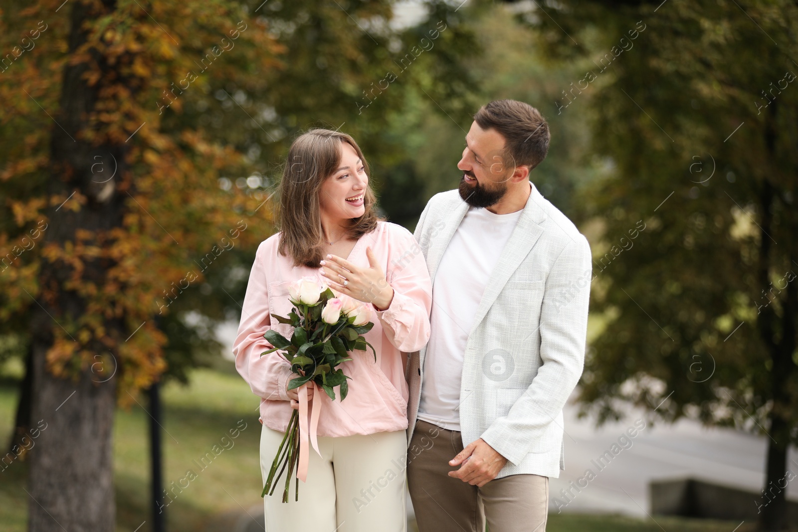 Photo of Making marriage proposal. Woman with engagement ring, flowers and her fiance outdoors