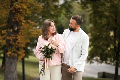 Photo of Making marriage proposal. Woman with engagement ring, flowers and her fiance outdoors