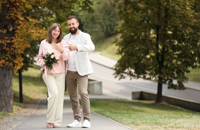 Photo of Making marriage proposal. Woman with engagement ring, flowers and her fiance outdoors, space for text