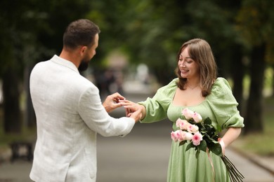 Photo of Making marriage proposal. Man putting engagement ring on his girlfriend's finger outdoors