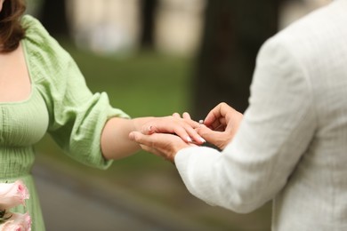 Photo of Making marriage proposal. Man putting engagement ring on his girlfriend's finger outdoors, closeup