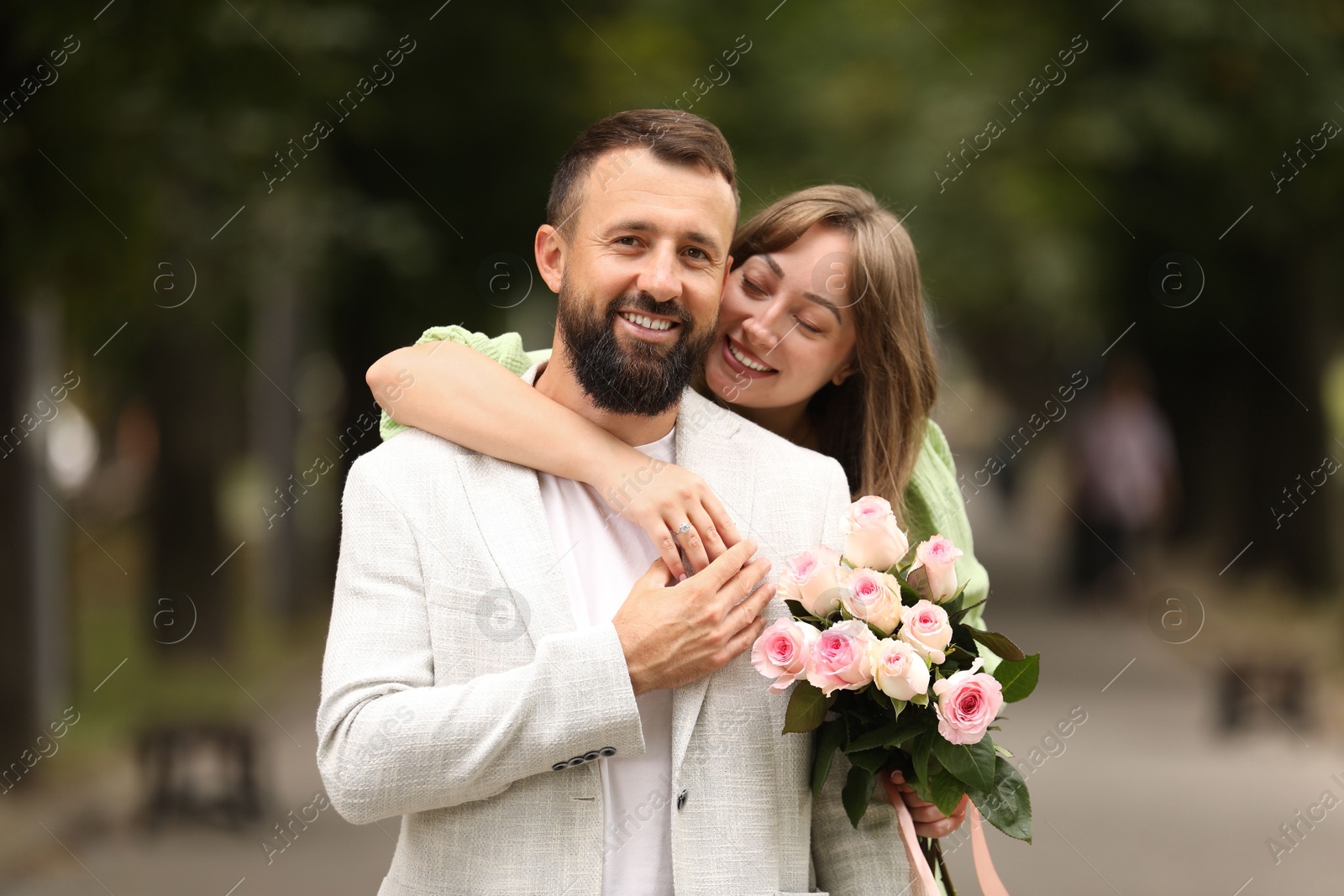 Photo of Making marriage proposal. Woman with engagement ring, flowers and her happy fiance outdoors