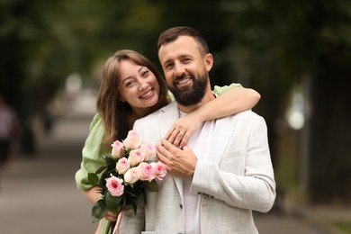 Photo of Making marriage proposal. Woman with engagement ring, flowers and her happy fiance outdoors