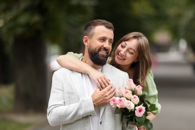 Photo of Making marriage proposal. Woman with engagement ring, flowers and her happy fiance outdoors
