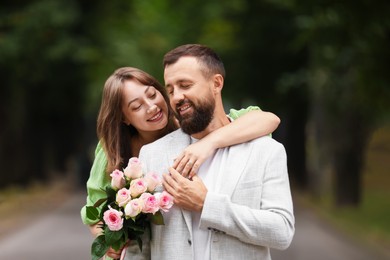 Photo of Making marriage proposal. Woman with engagement ring, flowers and her happy fiance outdoors