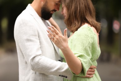 Photo of Making marriage proposal. Woman showing engagement ring and hugging her fiance outdoors, closeup