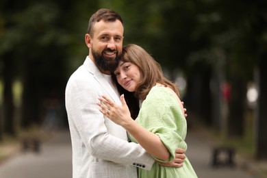 Photo of Making marriage proposal. Woman showing engagement ring and hugging her fiance outdoors