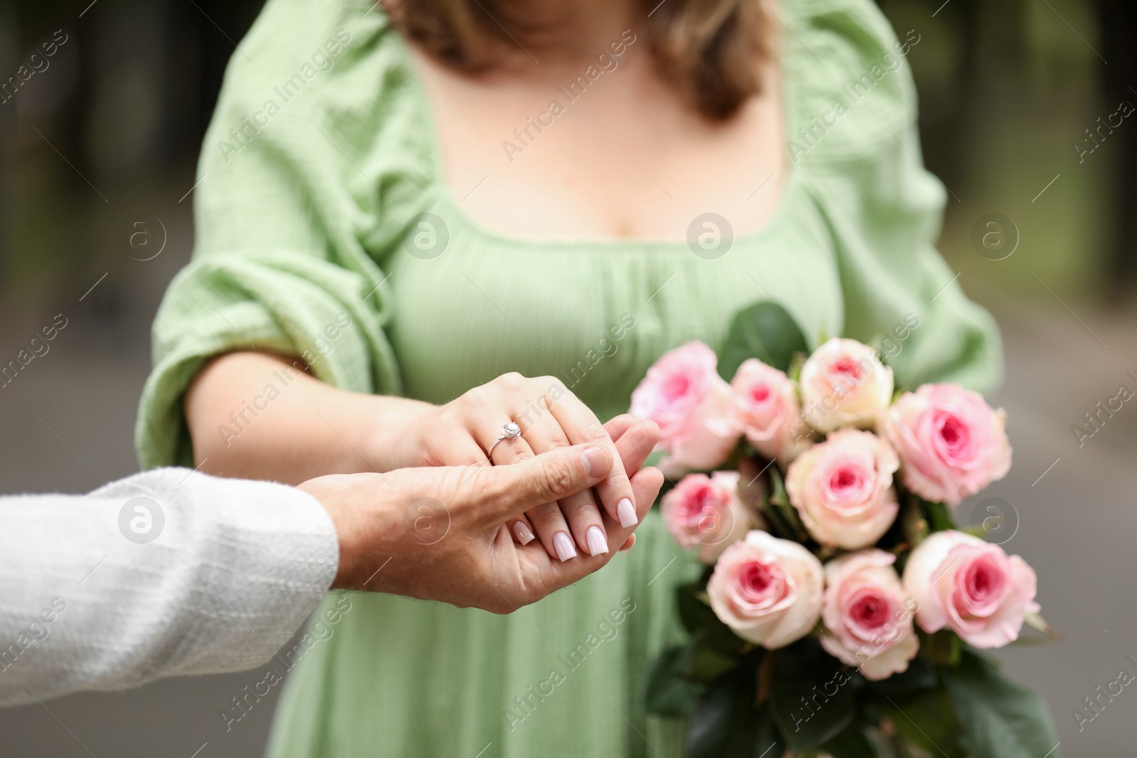 Photo of Making marriage proposal. Woman with engagement ring, flowers and her fiance outdoors, closeup