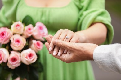 Photo of Making marriage proposal. Woman with engagement ring, flowers and her fiance outdoors, closeup