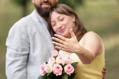 Photo of Making marriage proposal. Woman showing engagement ring and hugging her fiance outdoors, selective focus