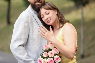 Photo of Making marriage proposal. Woman showing engagement ring and hugging her fiance outdoors