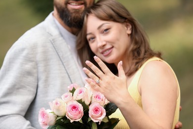 Photo of Making marriage proposal. Woman showing engagement ring and hugging her fiance outdoors, selective focus