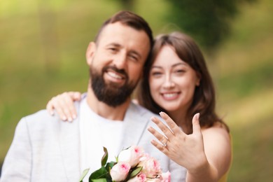 Photo of Making marriage proposal. Woman showing engagement ring and hugging her fiance outdoors, selective focus