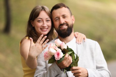 Photo of Making marriage proposal. Woman showing engagement ring and hugging her fiance outdoors, selective focus