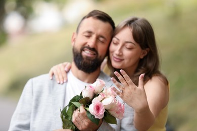 Photo of Making marriage proposal. Woman showing engagement ring and hugging her fiance outdoors, selective focus