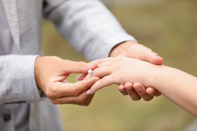 Photo of Making marriage proposal. Man putting engagement ring on his girlfriend's finger outdoors, closeup