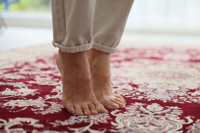 Photo of Woman barefoot on red carpet with pattern at home, closeup