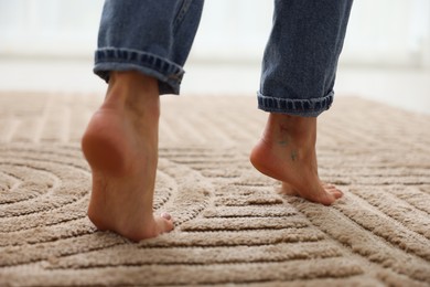 Photo of Woman walking barefoot on soft beige carpet at home, closeup