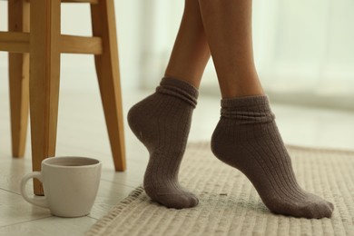 Photo of Woman in socks on soft beige carpet and cup at home, closeup
