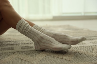 Photo of Woman in socks on carpet with pattern at home, closeup
