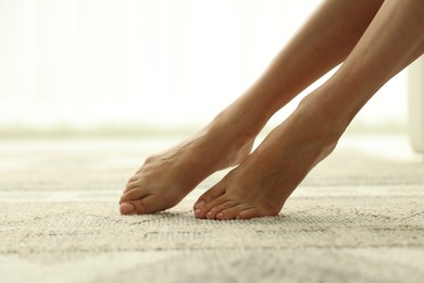 Photo of Woman barefoot on soft carpet with pattern at home, closeup. Space for text