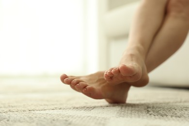 Photo of Woman barefoot on soft carpet with pattern at home, closeup. Space for text