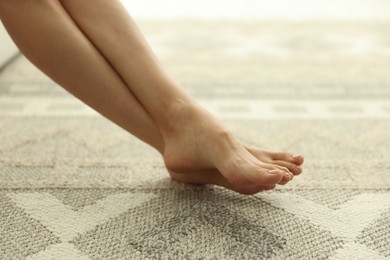 Photo of Woman barefoot on soft carpet with pattern at home, closeup