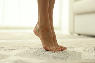 Photo of Woman barefoot on soft carpet with pattern at home, closeup