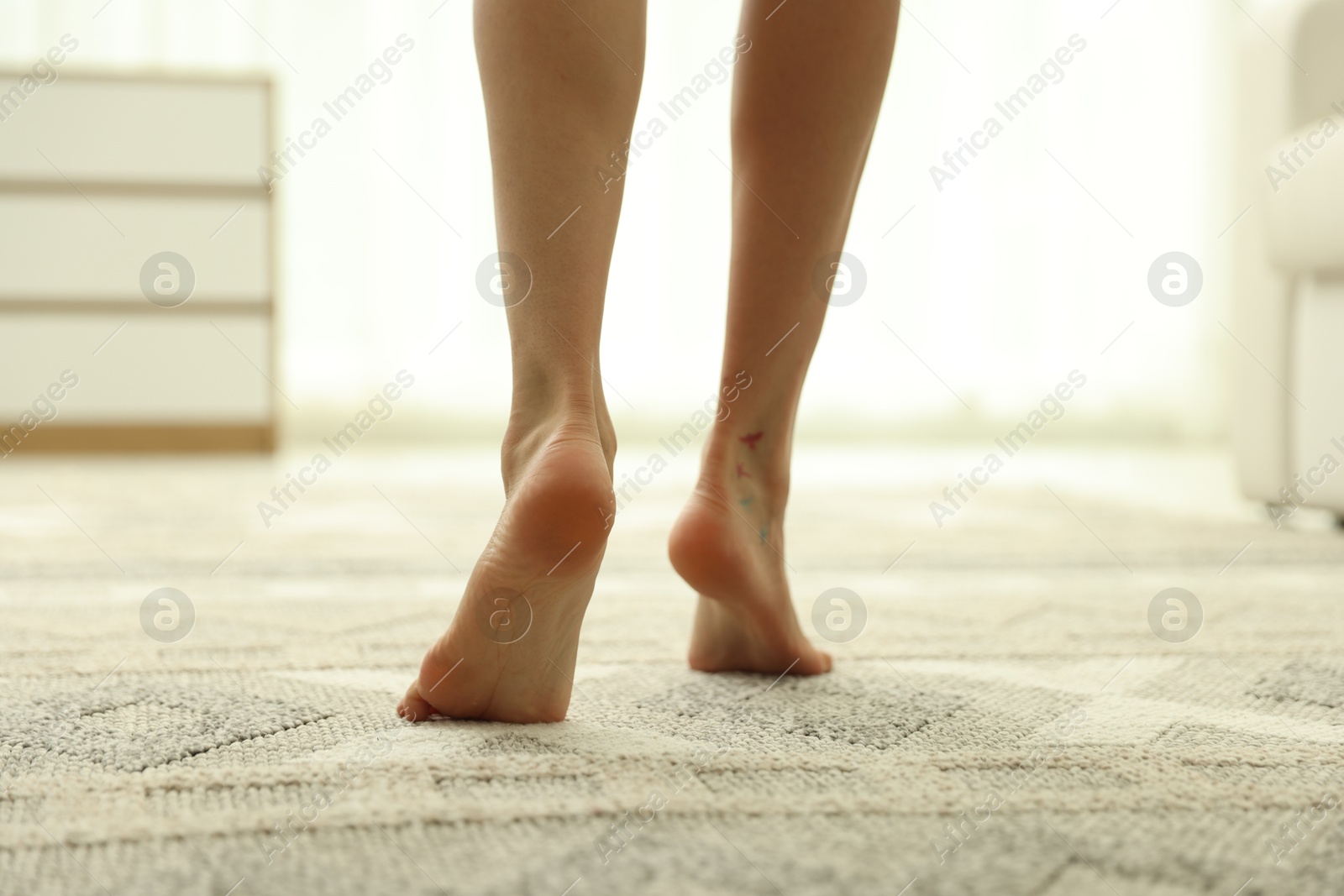 Photo of Woman walking barefoot on soft carpet with pattern at home, closeup