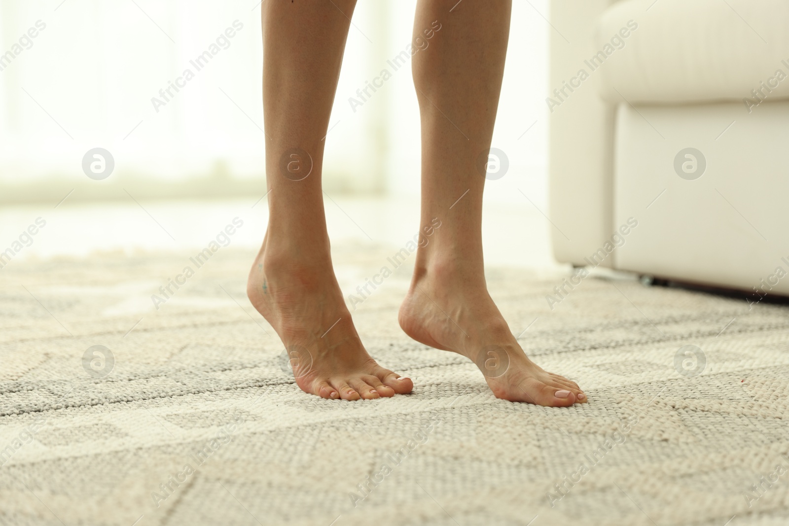 Photo of Woman walking barefoot on soft carpet with pattern at home, closeup