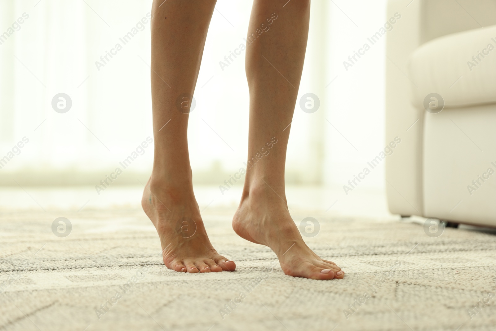 Photo of Woman walking barefoot on soft carpet with pattern at home, closeup
