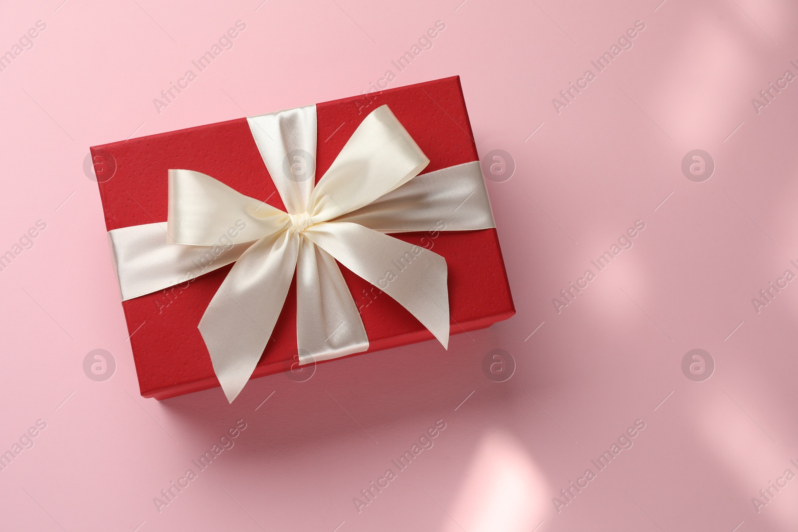 Photo of Beautiful gift box with bow on pink background, top view. Space for text