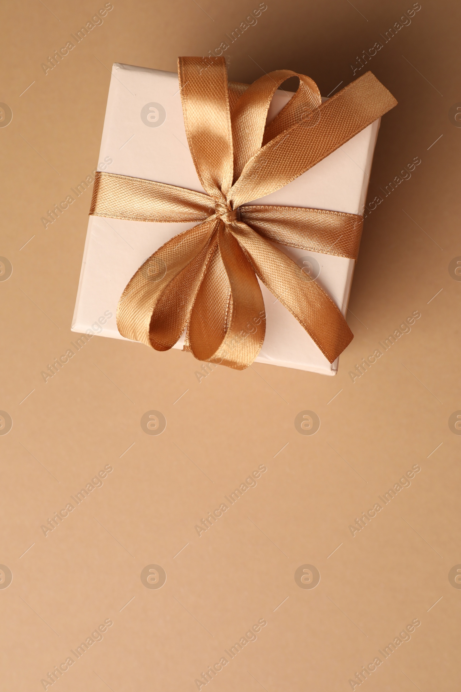 Gift box with beautiful bow on beige background, top view. Space for text Photo of Gift box with beautiful bow on beige background, top view. Space for text