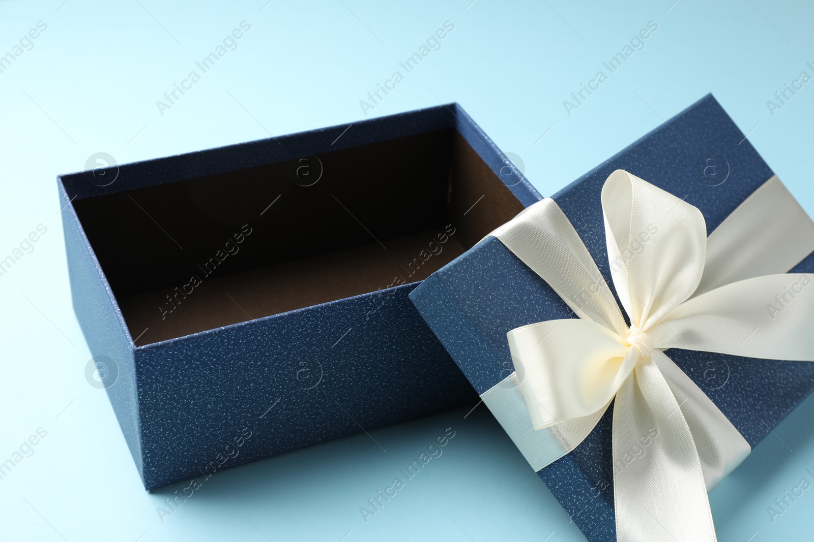 Photo of Opened gift box with beautiful lid on light blue background, closeup