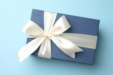 Photo of Gift box with beautiful bow on light blue background, top view