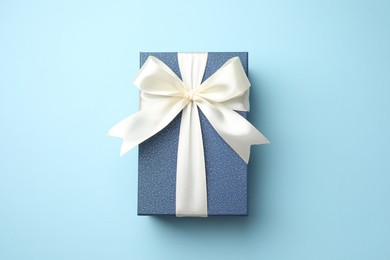 Photo of Gift box with beautiful bow on light blue background, top view