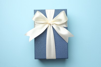 Photo of Gift box with beautiful bow on light blue background, top view
