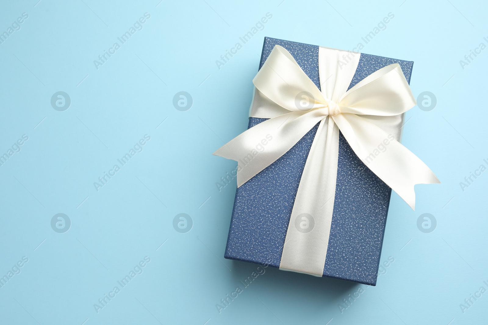 Photo of Gift box with beautiful bow on light blue background, top view. Space for text