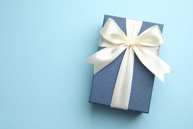 Photo of Gift box with beautiful bow on light blue background, top view. Space for text