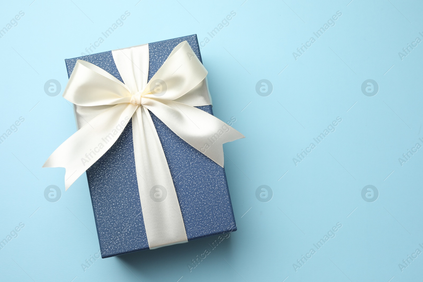 Photo of Gift box with beautiful bow on light blue background, top view. Space for text