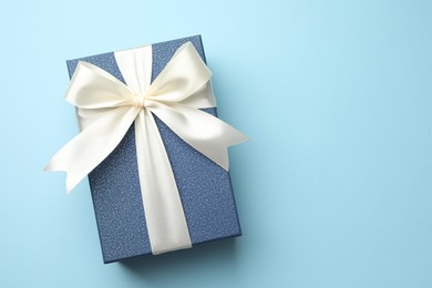 Photo of Gift box with beautiful bow on light blue background, top view. Space for text