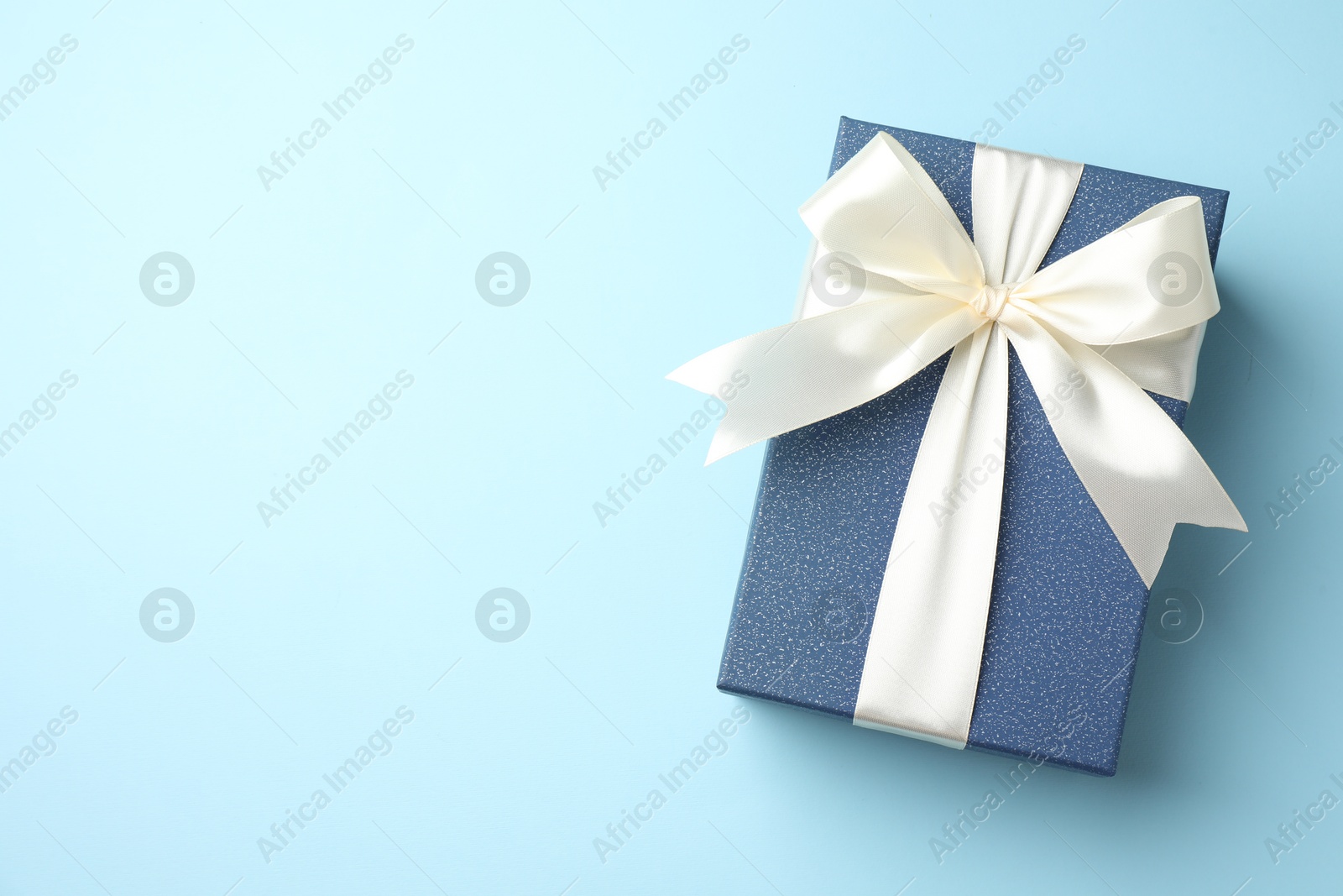 Photo of Gift box with beautiful bow on light blue background, top view. Space for text